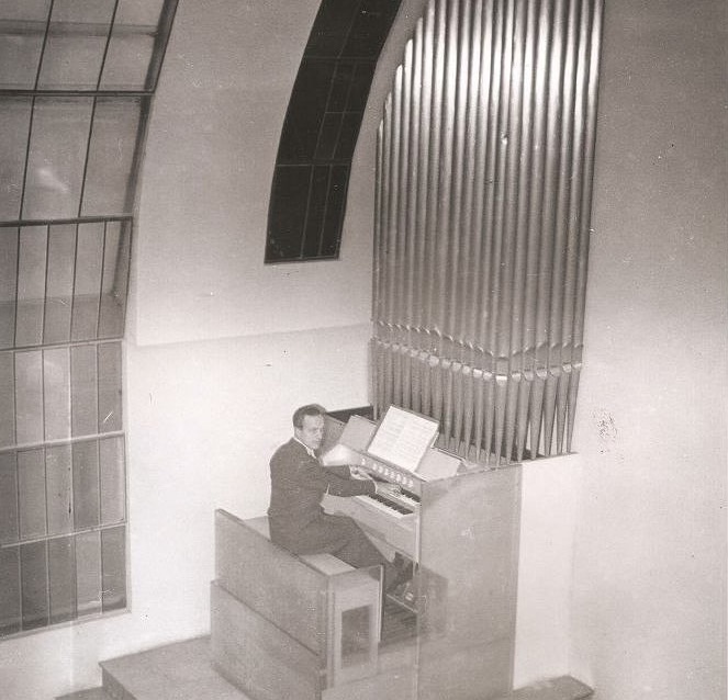 Man seen from above playing a big organ in a large white hallway.