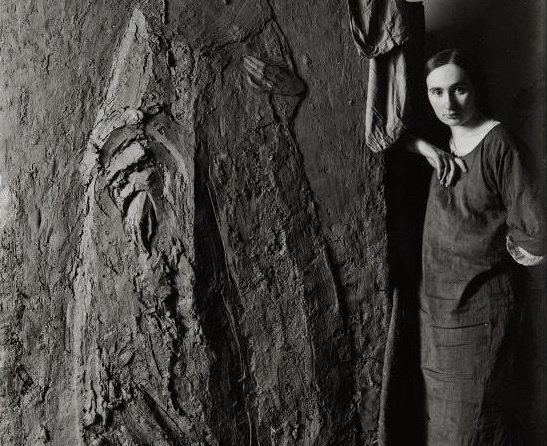 Woman early 1900s standing beside big art work/sculpture.