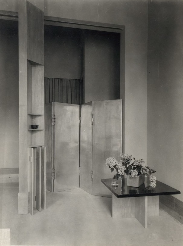 Boutique interior late 1920s. Black- and white photo. A photo in black and white of a boutique interior. A table in front with flowers on and a metal folding screen in the back
