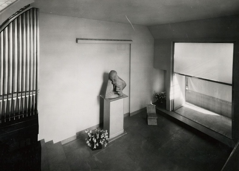 Light filled hallway. Big window with a balcony. Statue against a wall. Style 1920s.