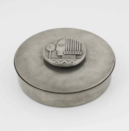 Metalwork tin jar by Sylvia Stave. On the handle image of face and a flower.