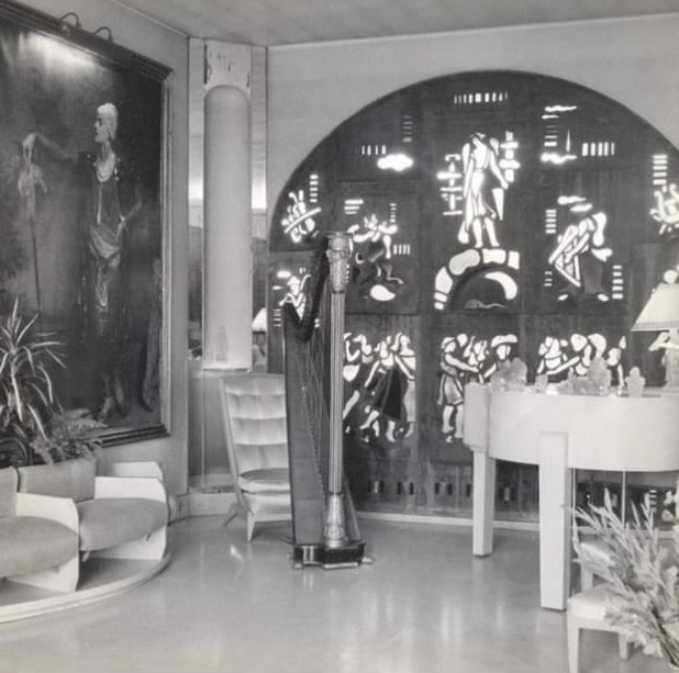 Interior of 1920s style living room. Balck and white photo. Big oil painting with man on the wall and a harp in the middle of the floor.
