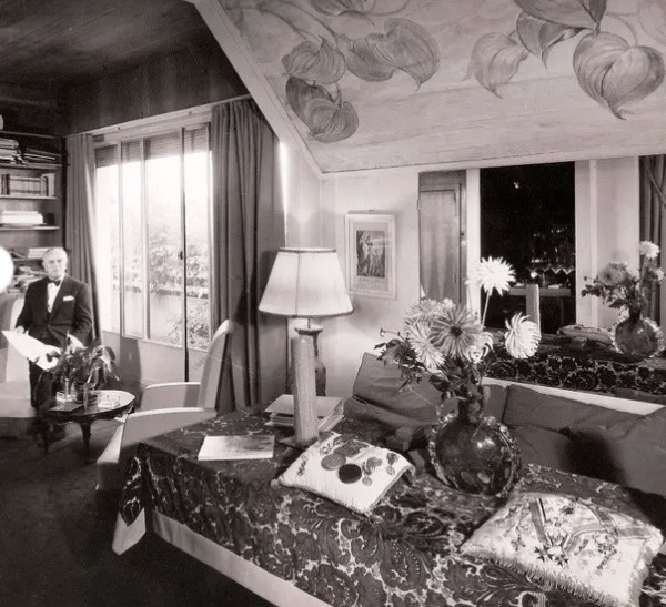 Livingroom interior, 1920s style. Man in the background in front of big window. Black and white photo.
