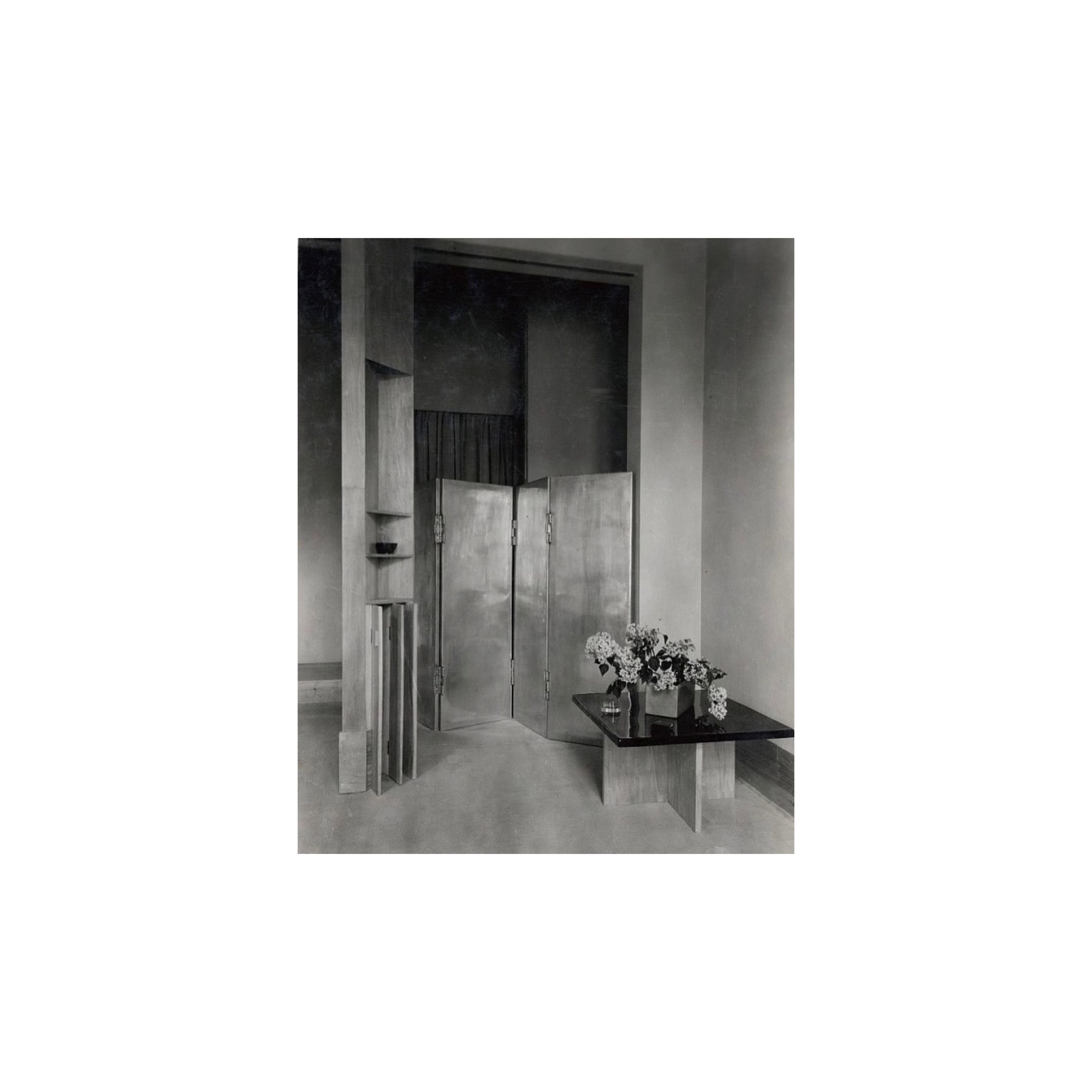 Boutique interior late 1920s. Black- and white photo. A photo in black and white of a boutique interior. A table in front with flowers on and a metal folding screen in the back.